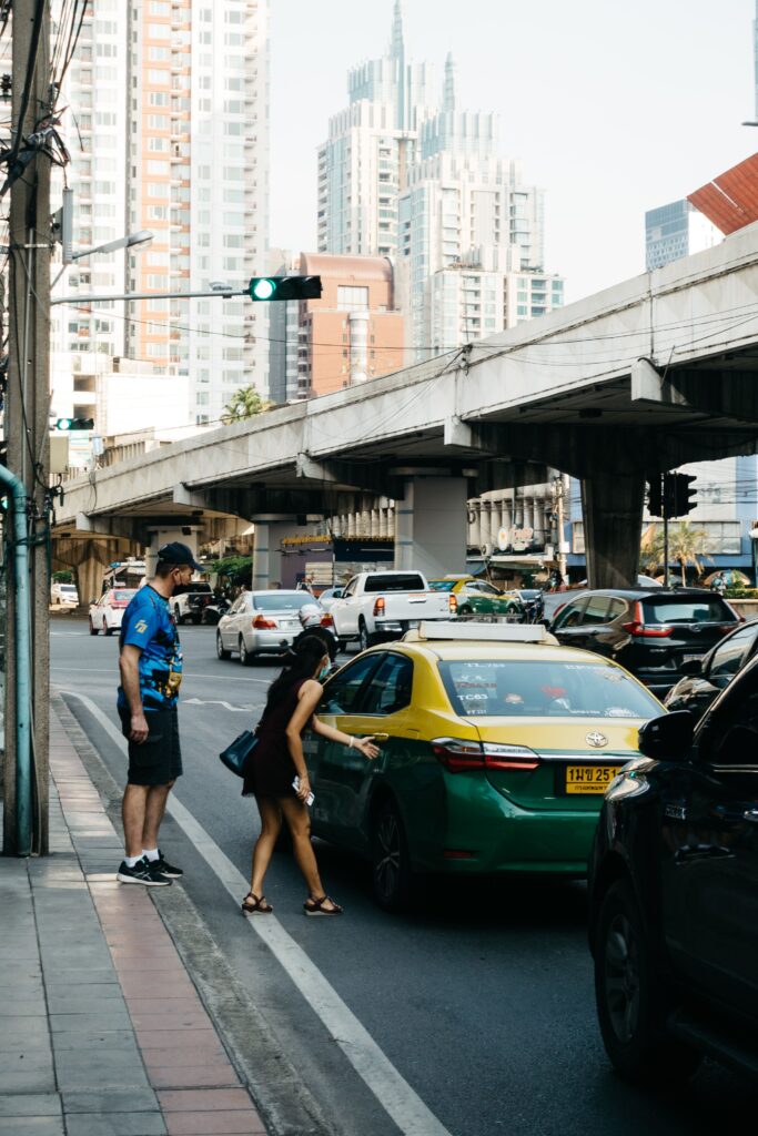 Tourists hailing a green and yellow metered taxi on a busy Bangkok street, demonstrating how to negotiate metered fares and avoid tourist scams in Thailand.