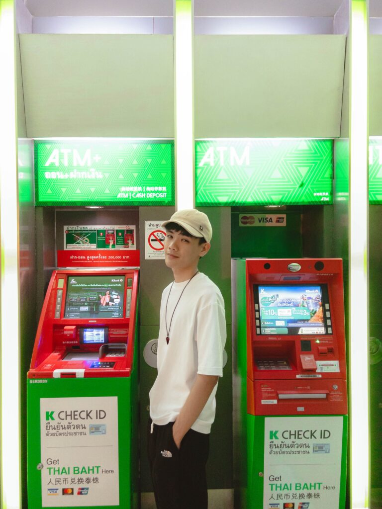 Traveler standing between green and red Kasikornbank (K-Bank) ATM and cash deposit machines to withdraw Thai Baht cash in Thailand.