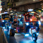 Colorful tuk tuks driving through a busy Bangkok street at night with glowing neon lights and tourists riding inside