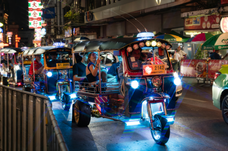 Colorful tuk tuks driving through a busy Bangkok street at night with glowing neon lights and tourists riding inside