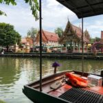 Traditional Thai temple beside a peaceful canal in Thailand with a wooden boat in the foreground and hidden local atmosphere away from tourist crowds.