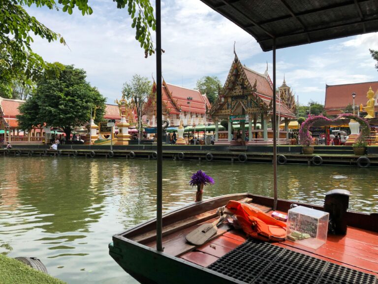 Traditional Thai temple beside a peaceful canal in Thailand with a wooden boat in the foreground and hidden local atmosphere away from tourist crowds.