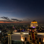 Wide angle evening to night view of Sky Bar at Lebua Bangkok rooftop bar with Bangkok skyline lights, luxury rooftop drinks, slow crowd atmosphere, and panoramic cityscape in Thailand.
