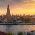 Wide angle sunset view of Wat Arun and the Phra Nakhon district in Bangkok Thailand with the Chao Phraya River and Bangkok skyline in cinematic golden light
