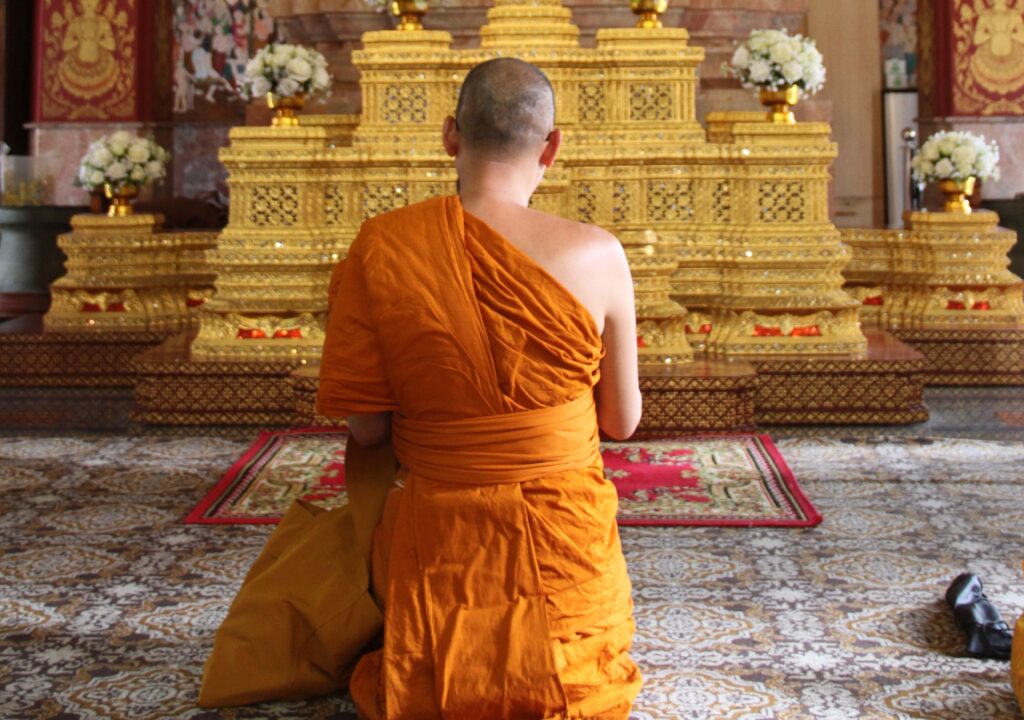 Buddhist monk praying in front of a golden Buddha statue inside a ornate temple hall in Bangkok, Thailand, representing spiritual wellness and mindfulness tourism