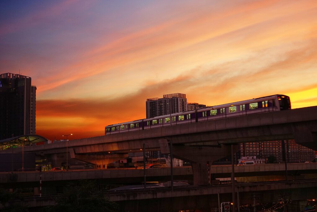 Urban transit in Bangkok at dusk, featuring a commuter train moving past high-rise apartment buildings under a dramatic golden hour sky.