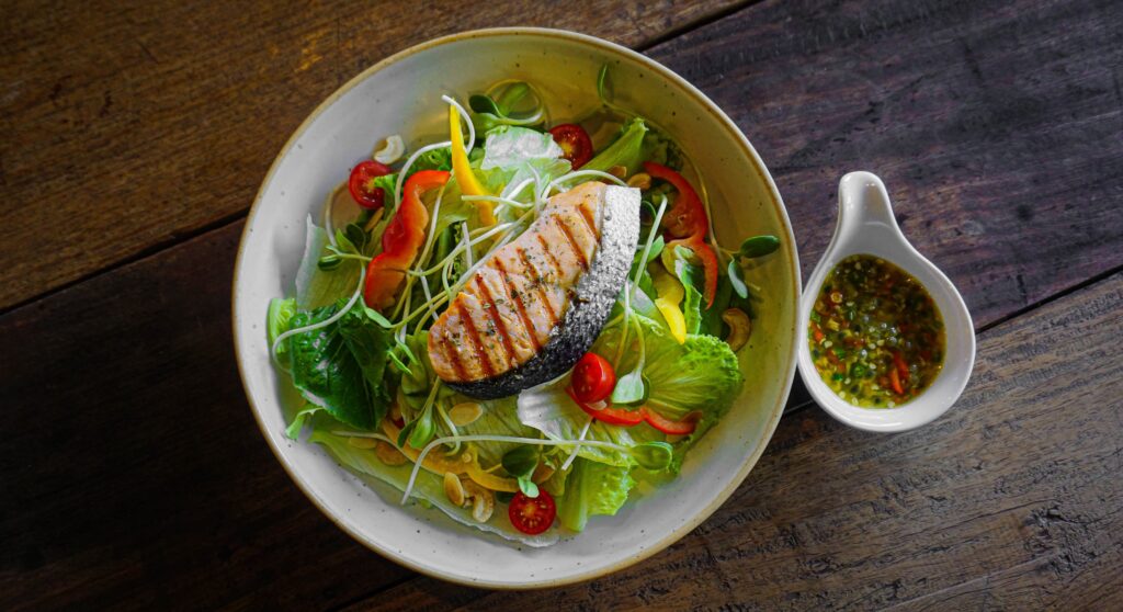 Nutritious grilled salmon salad with fresh greens and local dressing, showcasing healthy culinary options for wellness travelers in Bangkok, Thailand.