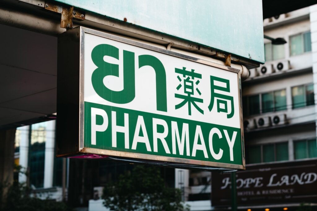 Street-level pharmacy sign in Bangkok with text in Thai, Chinese, and English, highlighting local healthcare and medical tourism infrastructure.
