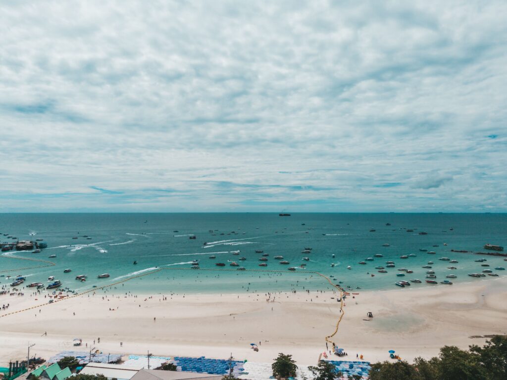 Aerial view of the expansive white sand and turquoise water at Pattaya Beach in Chon Buri, dotted with speedboats and swimmers, a popular coastal day trip from Bangkok.