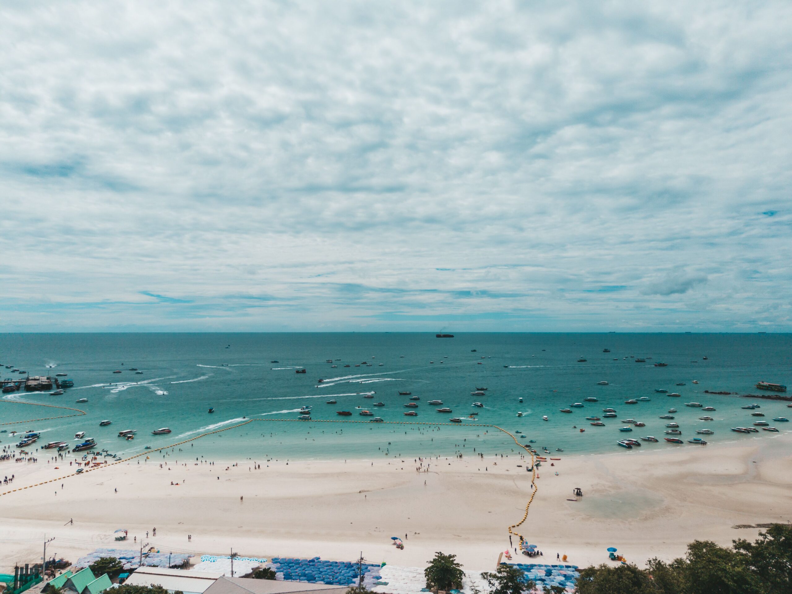 Aerial view of the expansive white sand and turquoise water at Pattaya Beach in Chon Buri, Thailand, filled with speedboats and swimmers, highlighting a top self-drive coastal day trip from Bangkok.