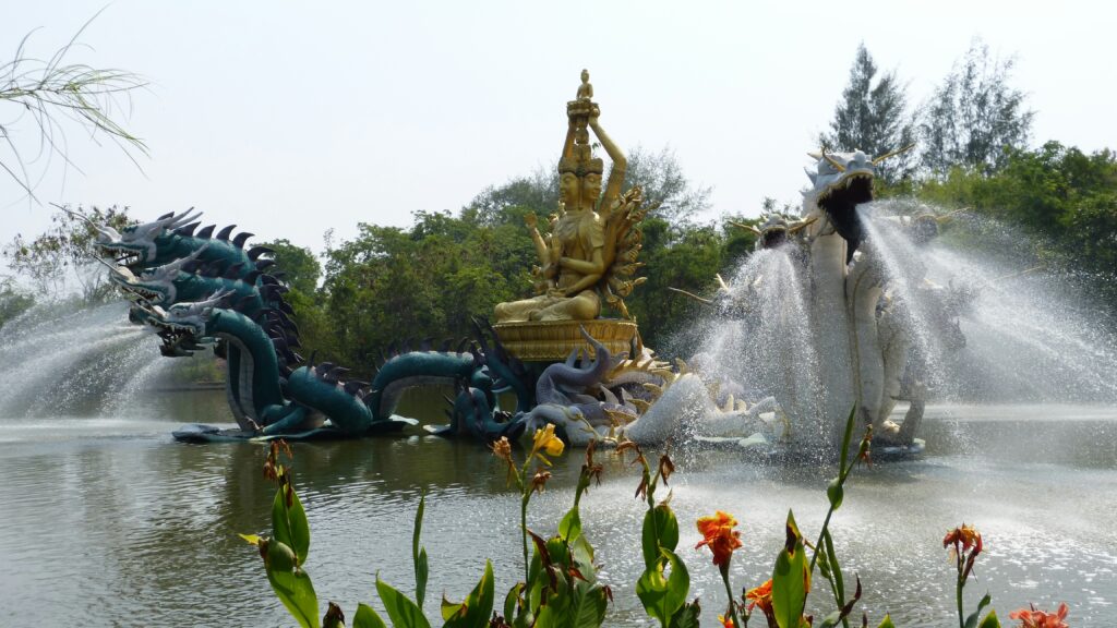 A massive fountain featuring a golden multi-armed deity and water-spouting mythical sea serpents in a lake at The Ancient City open-air museum, a top-rated Bangkok day trip in Samut Prakan.
