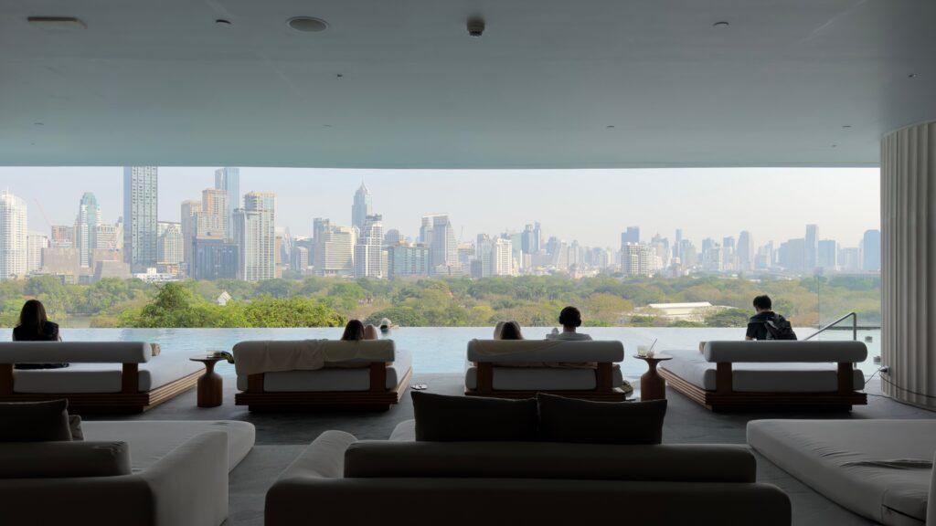 Relaxing luxury wellness lounge and infinity pool overlooking the Bangkok city skyline and lush park, representing wellness tourism in Thailand.