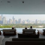 Relaxing luxury wellness lounge and infinity pool overlooking the Bangkok city skyline and lush park, representing wellness tourism in Thailand.